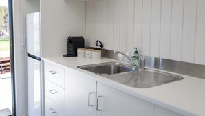 Une cuisine moderne avec un évier en acier inoxydable, des armoires blanches et une machine à café.