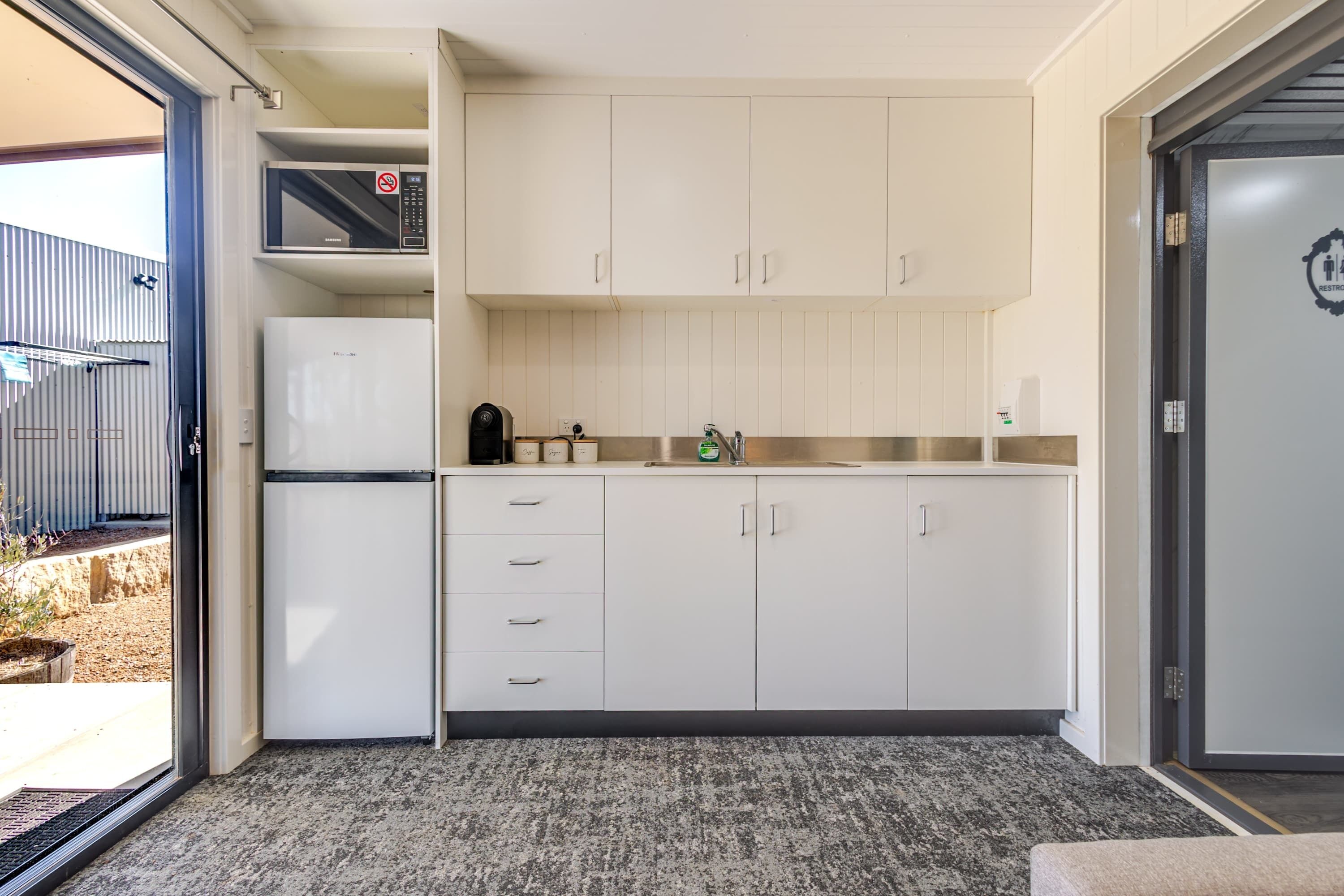 A compact kitchen with white cabinets, a built-in microwave, and a stainless steel sink.
