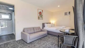 A hotel room with a bed, a sofa, a small table, a chair, and a window with curtains.