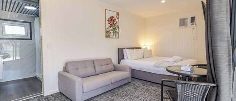 Habitación de hotel con cama, sofá, una mesita, una silla y una ventana con cortinas.