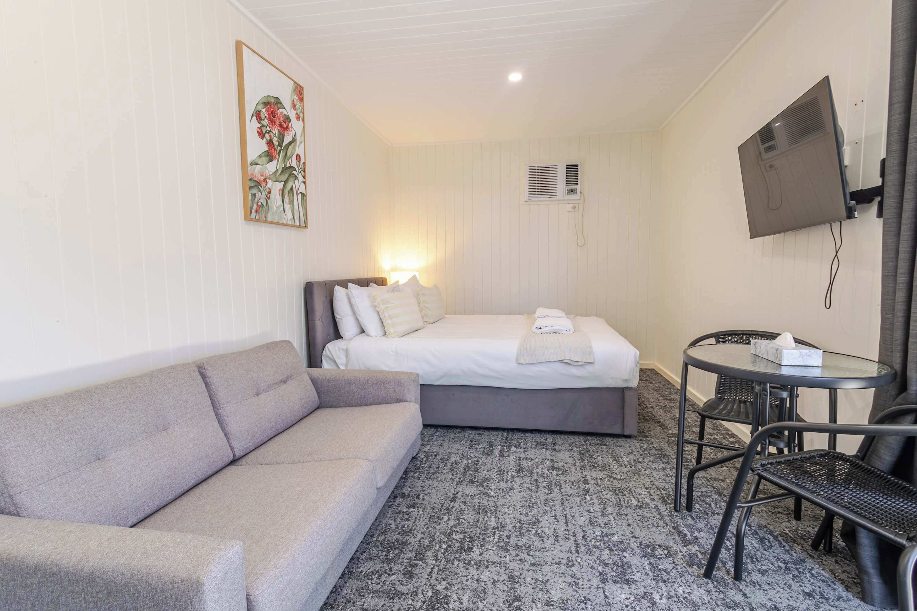 Ett hotellrum med en säng, en soffa, ett litet bord med stolar, en tv och en luftkonditioneringsanläggning.