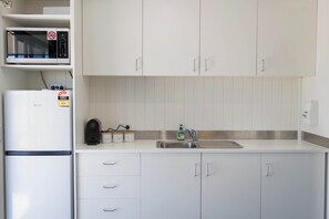 A kitchen with white cabinets, a microwave, a refrigerator, and a sink.