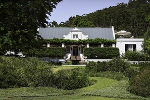 Um edifício grande e branco com fachada simétrica, entrada central com degraus e um jardim formal em primeiro plano.