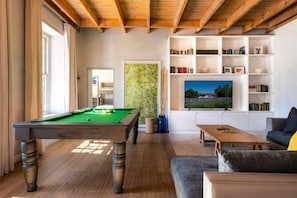 Ein Zimmer mit Billardtisch, Fernseher und Bücherregal.