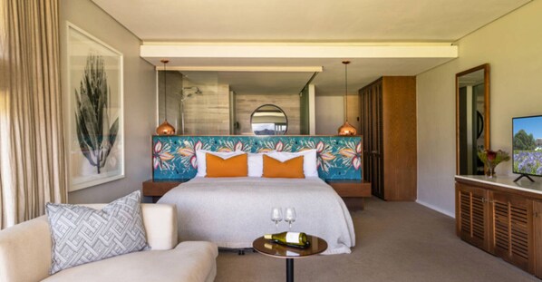 Ein Hotelzimmer mit einem großen Bett, einem Sofa, einem kleinen Tisch mit Gläsern, einem Fernseher und einem Spiegel.