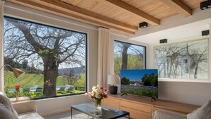 Uma sala de estar moderna com grandes janelas, uma TV de tela plana e vista para um vinhedo.