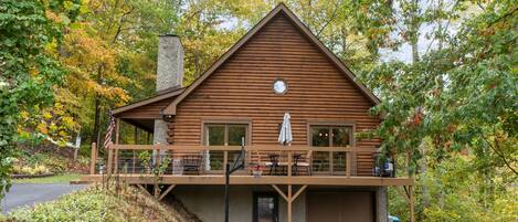Une cabane en rondins avec un balcon, un garage et une cheminée.