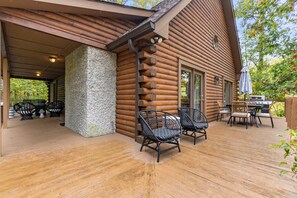 Eine Blockhütte mit überdachter Terrasse, Sitzgelegenheiten im Freien und einer Grillvorrichtung.