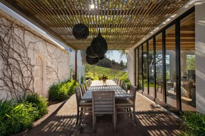 An outdoor dining area with a pergola overhead, a table with chairs, and a view of a vineyard. - Elegant Merlot Room with Captivating Panoramas 1038 (Western Cape)