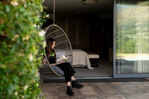 Eine Person sitzt in einer Hängematte und liest ein Buch, mit einem Bett und einer Glastür zu einem Garten.
