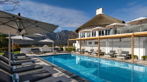 Ein Poolbereich mit Liegestühlen und Sonnenschirmen, ein klarer Himmel und Berge im Hintergrund.