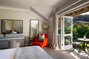 Hotelkamer met een bed, een bureau, een rode stoel, een balkon met een tafel en uitzicht op groen.