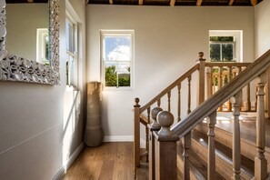 Eine Holztreppe mit Geländer, die zu einer oberen Etage führt, ein großer Spiegel mit aufwendiger Verzierung und ein Fenster mit Blick auf Grünflächen.