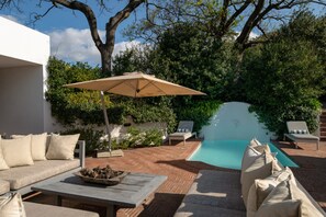 A poolside area with a lounge chair, a table with a bowl of pinecones, and an umbrella. - Elegant Shiraz Room with Vineyard & Mountain Views 1037 (Western Cape)