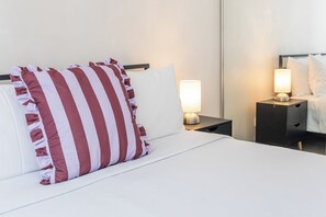 Une chambre d’hôtel avec un lit, deux tables de chevet et une petite table de nuit avec une lampe.