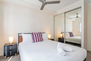 Ein Hotelzimmer mit Bett, Nachttischen, Deckenventilator, einem großen Spiegel und einem Fenster.