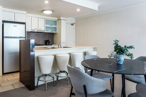 A modern kitchen with a built-in refrigerator, a stove, and a sink. There are four white bar stools and a round table with chairs. A potted plant is on the table. - Prime Loc River Glimpse 2BR Walk to CBD w/Parking (Brisbane City)