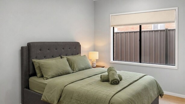 A bedroom with a bed, a nightstand, a lamp, and a window with blinds.