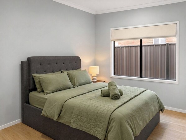 A bedroom with a bed, a nightstand, a lamp, and a window with blinds.