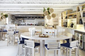 Un espace repas moderne avec des tables rondes, des chaises blanches et un bar doté d’étagères remplies de bouteilles.
