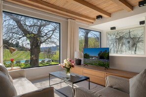A modern living room with large windows, a flat-screen TV, and a view of a vineyard. - Cap Classique Vineyard Pool Suites with Private Pool 1043 (Western Cape)