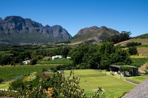 Cancha de tenis rodeada de exuberante vegetación y montañas al fondo.