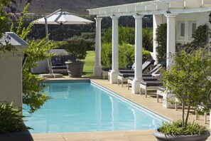 Un espace piscine agrémenté d’une pergola, de chaises longues et offrant une vue sur le paysage environnant.