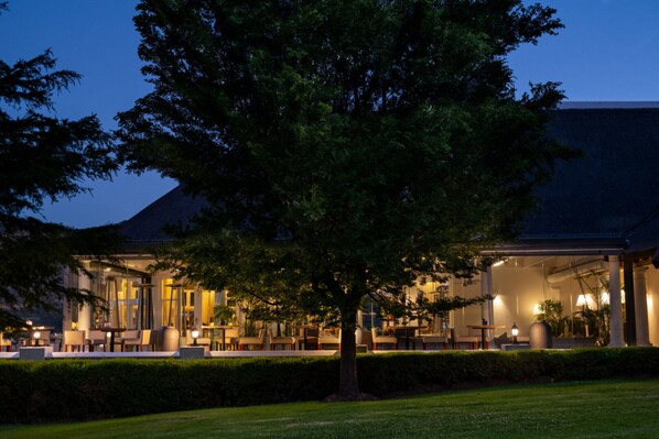 A hotel with outdoor seating, a large tree, and a well-lit entrance. - Chardonnay Room 1 with Manor Views 1044 (Western Cape)
