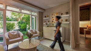 A modern living room with a sofa, a coffee table, and a kitchen area with wine glasses on display. - Chardonnay Room 1 with Manor Views 1044 (Western Cape)
