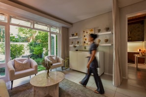 A modern living room with a sofa, a coffee table, and a kitchen area with wine glasses on display. - Chardonnay Room 1 with Manor Views 1044 (Western Cape)