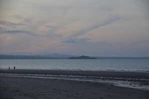 Ein Strand mit einer entfernten Insel und Bergen im Hintergrund.
