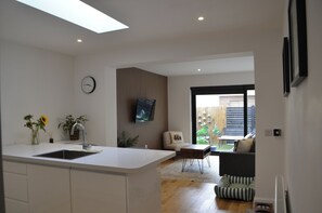 A modern kitchen with a central island, a dining area with a table and chairs, and a view of the outdoors through a sliding door. - 2BR Portobello Home by Beach with Garden (Edinburgh)