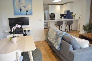 Een moderne woonkamer met een bank, een eettafel met een orchidee in pot, een televisie en een keuken op de achtergrond.