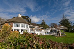 Une maison moderne à la forme circulaire et au toit de chaume, entourée d’un jardin bien entretenu et d’un espace extérieur aménagé pour se détendre.