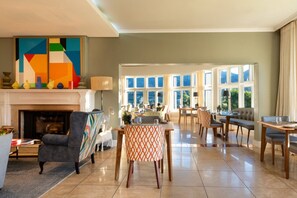 A spacious living room with a fireplace, a dining area with a table and chairs, and large windows offering a view of the outdoors. - Chardonnay Room 2 Light Filled Elegant En Suite 1045 (Western Cape)