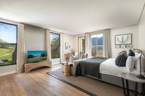 A bedroom with a large bed, a desk, a chair, a TV, and a view of the outdoors. - Chardonnay Room 2 Light Filled Elegant En Suite 1045 (Western Cape)
