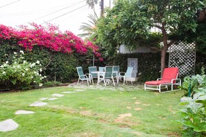 Eine Terrasse mit Tisch und Stühlen, umgeben von üppigem Grün und blühenden Pflanzen.