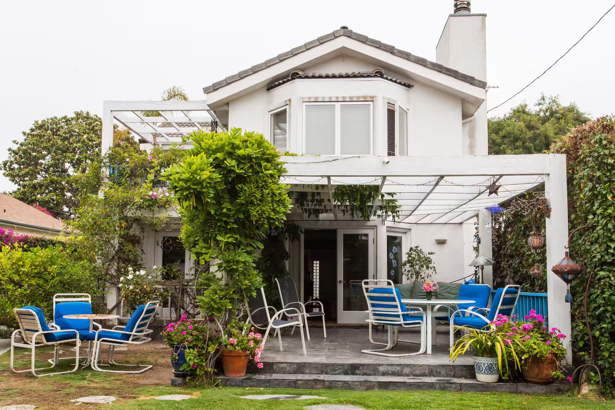 Een huis met een overdekte patio, buitenmeubilair en plantenpotten.