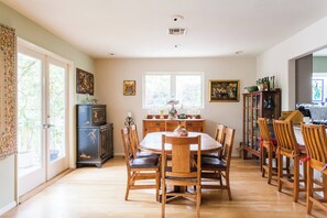 Un comedor con una mesa redonda y sillas de madera, un aparador con objetos decorativos y una ventana con luz natural.
