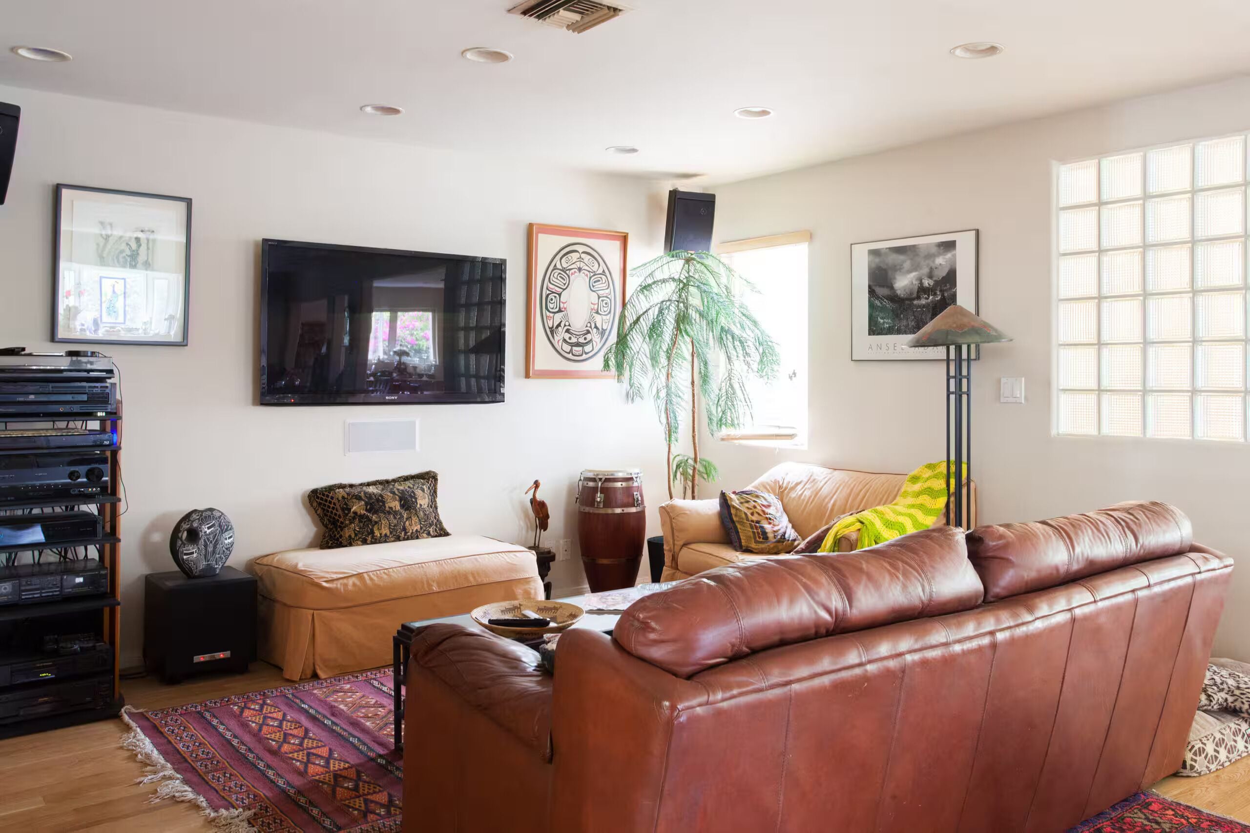 A living room with a leather sofa, a flat-screen TV, a drum, and a large window.