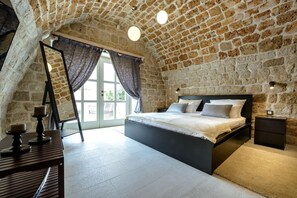A bedroom with a stone wall, a bed, a nightstand, a dresser, and a window with curtains. - Villa Tihomira - Private villa with pool, Dalmatia (Zaton)