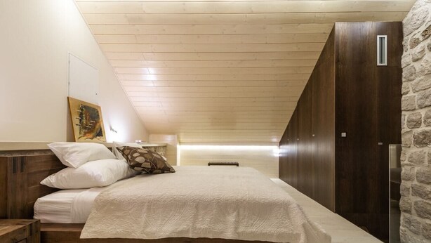 Un dormitorio con una cama de madera, una mesita de noche, una pared de piedra y un techo inclinado.