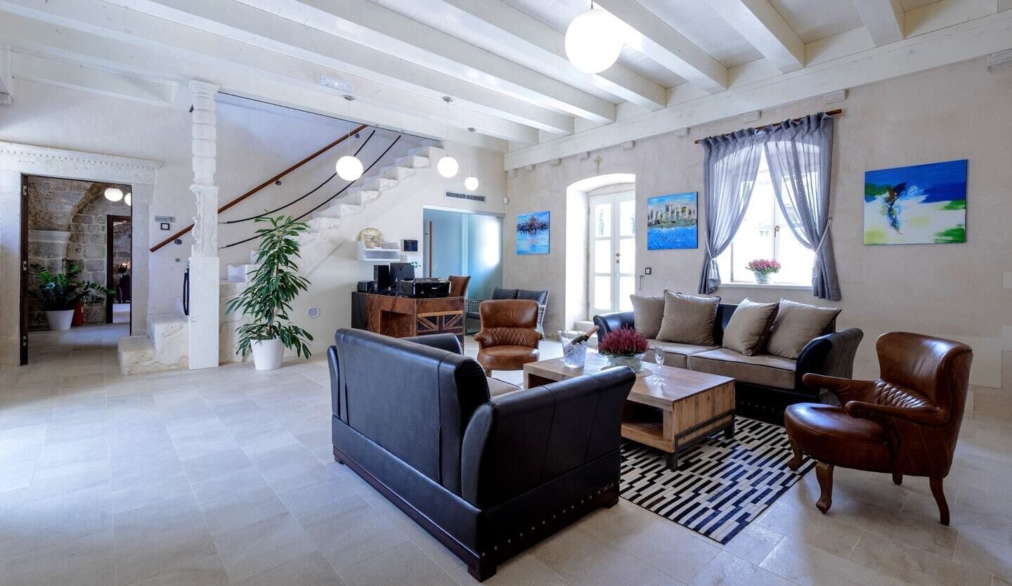 Uma sala de estar ampla com um sofá, poltronas e uma mesa de centro. Escada leva a outro nível, e uma grande janela com cortinas.