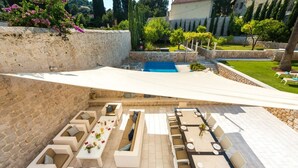 Un patio al aire libre iluminado por el sol, con paredes de piedra, una piscina y áreas de estar exteriores.