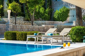 En swimmingpool med solstolar och en stenmur.