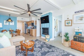 A living room with a sofa, coffee table, and a fireplace. There is a kitchen in the background with a microwave and cabinets. - Luxurious Coastal Oceanfront Suite! Yachtsman 601 (Myrtle Beach)