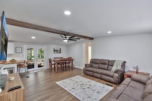 A spacious living area with a large brown sofa, a dining table with chairs, a ceiling fan, and a view through a glass door. - 25 minutes from Clemson, newly remodeled home! (Seneca)