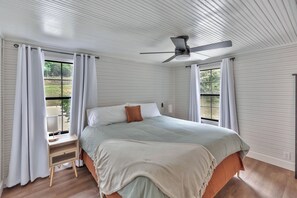 Ein Schlafzimmer mit einem Bett, Deckenventilator und fensterbepflanzten Fenstern.