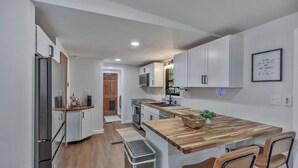 A modern kitchen with white cabinetry, a wooden countertop, stainless steel appliances, and a bar area with two stools. - 25 minutes from Clemson, newly remodeled home! (Seneca)