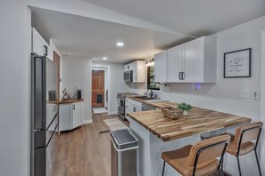 A modern kitchen with white cabinetry, a wooden countertop, stainless steel appliances, and a bar area with two stools. - 25 minutes from Clemson, newly remodeled home! (Seneca)